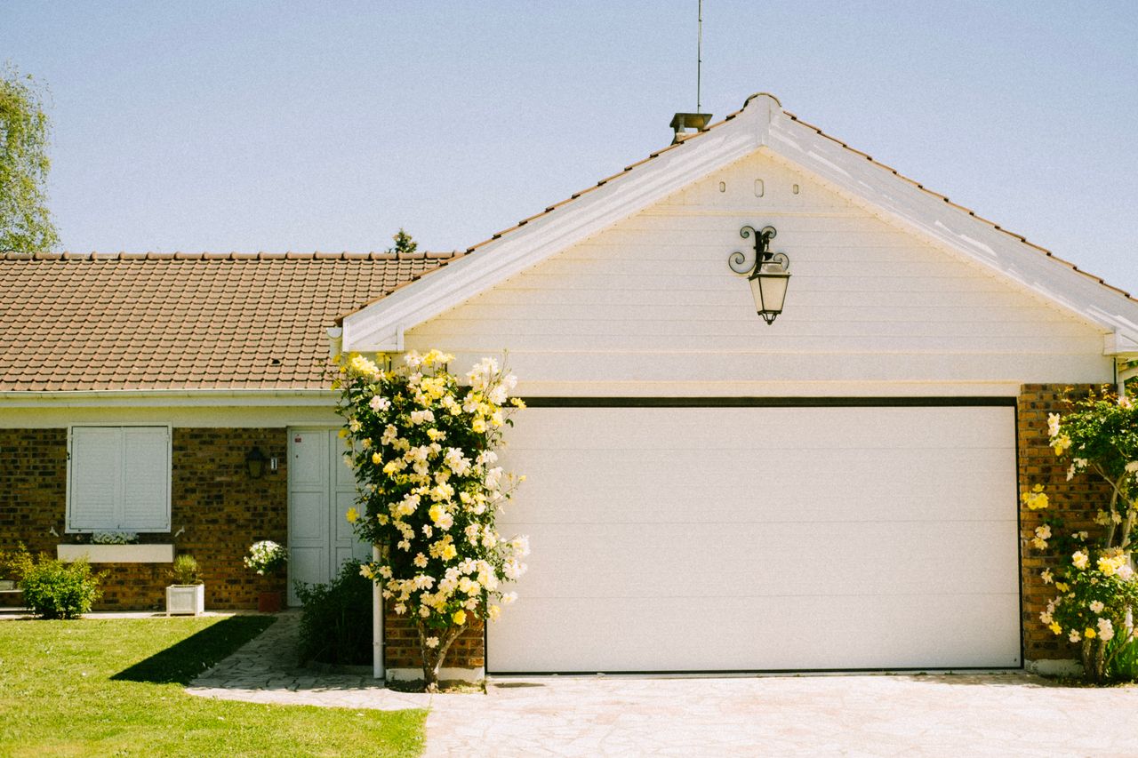 Home with well-maintained garage door surrounded by flowering plants